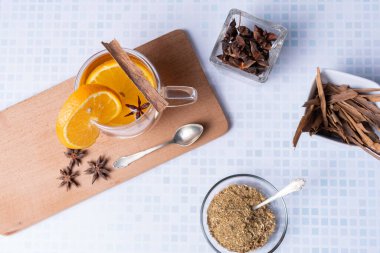 Üzerinde papatya, tarçın, portakal ve anason çiçekleri olan cam bardağın üst görüntüsü..