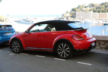 Monte-Carlo, Monaco - 16 Nisan 2023: Vibrant red 2019 Volkswagen Beetle R-Line üstü açık, siyah yumuşak üstü açık, Monte-Carlo caddesinde arka planda yatlar, yan görüş