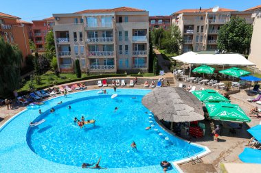 Sunny Beach, Bulgaristan - 8 Ağustos 2019: Güneş pansiyonları ve şemsiyelerle çevrili büyük bir yüzme havuzunun yer aldığı canlı bir tatil beldesi. Aileler ve arkadaşlar havuzun tadını çıkarıyorlar ve tatil atmosferinde dinleniyorlar.
