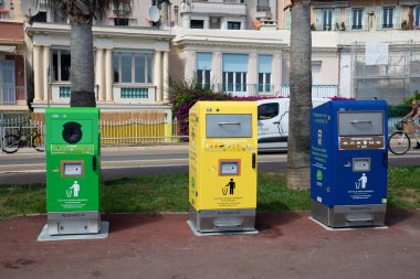 Nice, Fransa - 12 Haziran 2024: Promenade des Anglais 'te cam, ambalaj ve çeşitli atıklar için üç renkli geri dönüşüm kutusu düzgünce düzenlenmiştir. Çöp bidonları yeşil, sarı ve mavidir. Toplumda geri dönüşümü teşvik ederler. Konut inşaatı