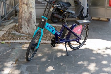 Nice, Fransa - 12 Haziran 2024 Nice 'te kaldırıma park etmiş mavi ve mor bir midilli bisikleti. Bisiklet, bisiklet paylaşım programının bir parçası, bir ağacın yanında duruyor ve kullanıma hazır, kentsel hareketlilik çözeltisi sergiliyor