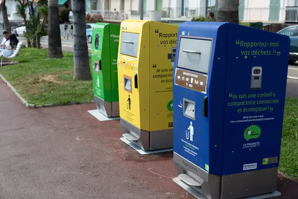 Nice, Fransa - 12 Haziran 2024: Gezinti güvertesinde cam, ambalaj ve çeşitli atıklar için renkli geri dönüşüm kutuları düzenlenmiştir. Çöp bidonları yeşil, sarı ve mavi renkli olup, toplumda geri dönüşüm ve çevre sorumluluğunu teşvik etmektedir.