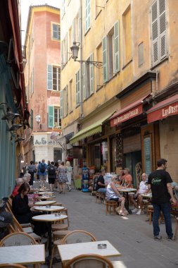 Nice, Fransa - 12 Haziran 2024: Eski Nice kasabasında renkli binalar ve açık hava kafelerle dolu canlı ve büyüleyici bir cadde. İnsanlar eğleniyor, masalarda oturuyorlar ve yayalara yakın yerlerde geziniyorlar.