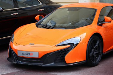 Monte-Carlo, Monaco - 28 Mayıs 2016: Lüks bir arabanın yanına park edilmiş turuncu bir McLaren 650S, lüks tasarımı ve aerodinamik eğrileri sergiliyor. Süper araba, yüksek performanslı otomotiv mühendisliğinin çarpıcı bir örneğidir.