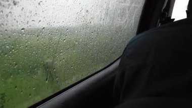 Yağmurda bir araba penceresinin yanında oturan bir adamın görüntüsü, pencerede yağmur damlaları var. Sinematik öykülerde, yolculuk videolarında veya dramatik anlarda kullanıma uygundur..