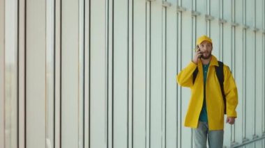 Sarı Üniformalı Genç Yemek Teslimatçısı ve Modern Ofis Binasında Termal Sırt Sırtçantasıyla Yürüyen ve Akıllı Telefon Kullanarak Sipariş Veren. Kurye siparişi bir müşteriye ulaştırmak üzere yolda..