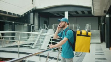 Fast Food Teslimat Adreslerini Ararken Akıllı Telefon Kullanan Yemek Teslimatçısı. Sarı Üniformalı Gıda Teslimatçısı ve Sırt çantalı Akıllı Telefon kullanarak siparişi kontrol ediyor. Hızlı teslimat.