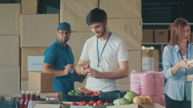 Yardım, Bağış ve Gönüllü Yardım Konsepti - Mutlu Gülümseyen Gönüllüler Grubu Dağıtım veya Mülteci Yardım Merkezi 'ndeki kutularda yiyecek paketliyor. Gönüllü Depo