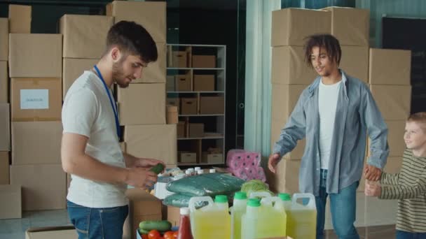 在分发或难民援助中心的友好志愿者捐赠盒和食物给人和他的儿子 社会援助概念 国内流离失所者 — 图库视频影像