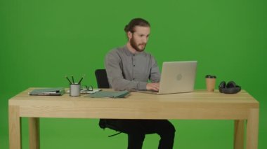 Genç Motivasyonlu Sakallı Adam Serbest Çalışan Öğrenci Çevrimiçi Tahta Masa Projesi üzerinde çalışıyor ve Yeşil Ekran 'da Gülümseyen Kamera' ya bakıyor, Chroma Key. Çevrimiçi Çalışma Konsepti Başarılı