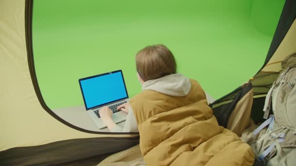 緑の画面 クロマキー 女性のキャンパーは ブランクブルースクリーンとラップトップでオープンテントに横たわっています テント内からの眺め 自然の中でのリモートワーク 友人とのチャット またはサイトの閲覧 — ストック動画
