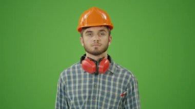 Yeşil Ekran. Genç Sakallı İnşaat Mühendisi Kareli Gömlek, Sert Şapka, İş Eldiveni ve Deri Alet Kemeri Giyiyor, Dairesel Testereyi Kaldırıyor, Hareketi onaylıyor ve Kameraya Gülümsüyor