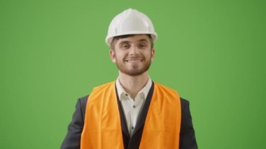 Yeşil Ekran. Genç Sakallı İnşaat Mühendisi 'nin portresi Siyah Klasik Takım Giyen, Beyaz Şapka ve Güvenlik Ceketi Katlanmış Silahlarla Duran ve Kameraya Bakan Gülümseyen Modern İnşaatçı Konsepti