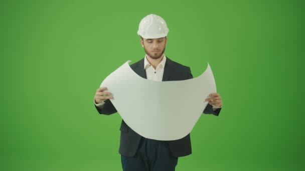 绿色屏风 年轻胡子土木工程师身穿黑色经典西装 头戴白色硬帽的肖像 展开蓝图 环视四周的笑容 现代建筑概念 — 图库视频影像