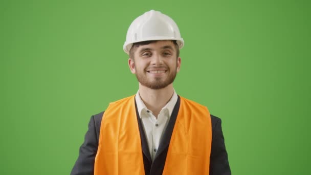 绿色屏风 年轻胡子土木工程师身穿黑色经典西服 白色硬帽衫 安全夹克 手持折叠式臂架 望着相机微笑的肖像 现代建筑商概念 — 图库视频影像
