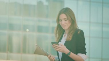 Genç Başarılı İş kadınının portresi Takım Elbiseli, Modern Cam İş Bölgesi 'ne Yakın Yürüyen ve Akıllı Telefon Kullanan. Takım Elbiseli Kadın Akıllı Telefonla İyi Haberler Veriyor.