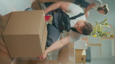 Dikey video. İşçi İşçi Mühürleme Karton Kutusu Koli Bant Makinesi kullanıyor. Profesyonel Paketleme ve Boşaltma Hizmetleri. Taşınmak için toplanma ve hazırlık. Malzemeler ve Malzemeler Paketleniyor