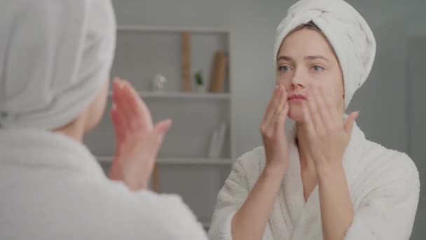 動揺した女の後ろ姿が鏡を見て顔にクリームを塗る 顔のしわの問題とにきびについてストレスを感じる悲しい若い女性 化粧品の現代技術の概念 — ストック動画