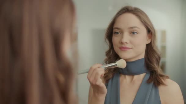 鏡の前にブラシで粉末を適用する可愛い女性のバックビュー イベントの準備中に彼女の顔に化粧を適用ドレスで魅力的な女性 美容業界の概念 — ストック動画