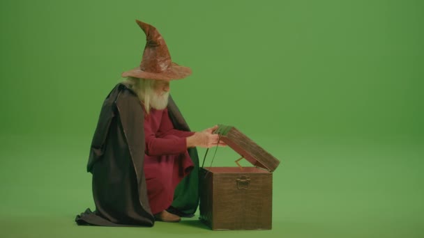 一个穿着中世纪服装和魔法帽的老魔法师打开了魔法的胸膛 拿出了魔法魔杖 等待奇迹 魔法物品 魔法盒 镜子和其他人工制品 — 图库视频影像