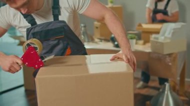 İşçi İşçi Mühürleme Karton Kutusunu Koli Bant Makinesi ile Kapatıyoruz. Profesyonel Paketleme ve Boşaltma Hizmetleri. Taşınmak için toplanma ve hazırlık. Malzemeler ve Malzemeler Paketleniyor