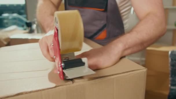 従業員のクローズアップダクトテープマシンを使用して段ボール箱を密封します 専門的な梱包と梱包解除サービス 移動のための梱包と準備 梱包資材 — ストック動画