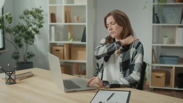 集中女性は突然首の痛みを感じるノートパソコンとテーブルで動作します 長いセメントライフスタイルの疲れを感じる女性は マッサージネックをこすりで痛みを緩和し 緩和しようとします オフィス症候群 — ストック動画