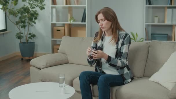 動揺した女性は家に座っている間に静止した水のガラスを飲むことによって頭痛のための丸薬を取ります インフルエンザの症状 健康管理 病気のための薬 — ストック動画