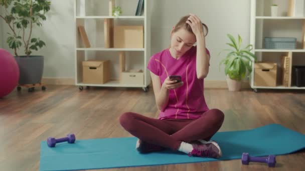 自宅で朝の運動中にワークアウトの間にスマートフォンを使用してフィット女性の肖像画 健康的なライフスタイル フィットネス レクリエーション — ストック動画