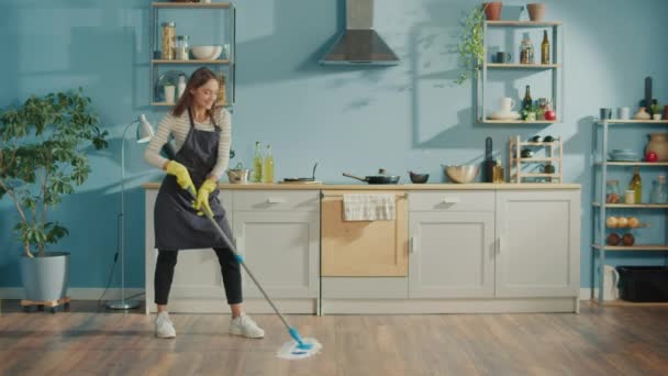 有创意的女人在家里用拖把洗地板 在厨房里跳舞 快乐的年轻女人可爱的家庭主妇在做家务的时候听音乐和跳舞 家务概念 — 图库视频影像