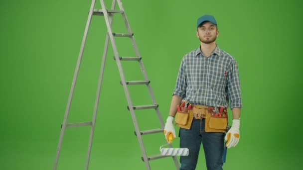 绿色屏风 年轻而有自信的土木工程师 身穿格子衬衫 蓝帽和皮革工具带 高举漆辊 做得很好 看着楼梯附近的相机微笑 — 图库视频影像