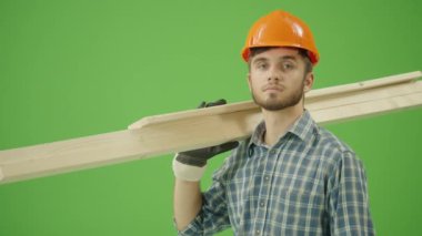 Yeşil Ekran. Genç Sakallı İnşaat Mühendisi Kareli Gömlek Giyiyor, Sert Şapka Giyiyor, İş Eldiveni Giyiyor, Omuzlarda Ahşap Kalaslar Tutuyor, Hareketleri onaylıyor ve Kameraya Gülümsüyor