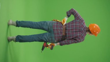 Dikey Görüntü. Yeşil Ekran. Geri Bakış. Checkered Shirt, Miğfer, Alet Kemerli Genç Kendine Güvenen Kadın Mimar, Eldeki Matkap, Şapka Düzeltme, Etrafa Bakış. Kadın İş Konsepti.