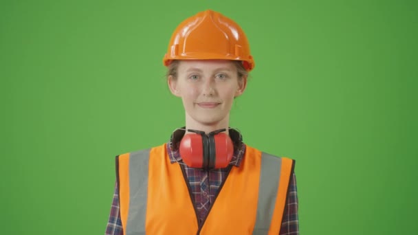 绿色屏风 身穿格子衬衫 防弹衣 助听器及工作服 升降圆锯 微笑及制造吊篮的年轻女建筑工人 建筑工人快乐概念 — 图库视频影像