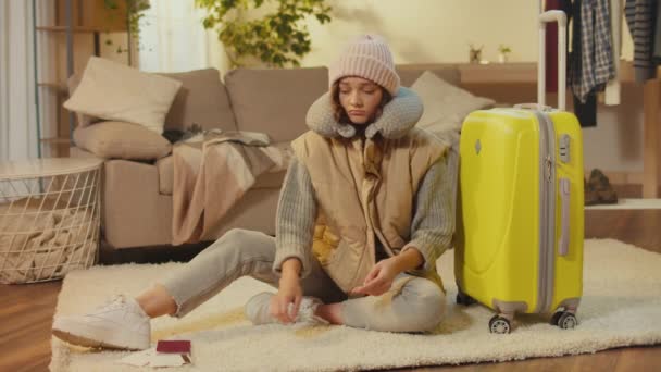 スーツケースを着た帽子の若い女性がカーペットの上に座っています 悲しい女性旅行者は 成功しない旅行に不満があります 失われた文書 ビザの問題 — ストック動画