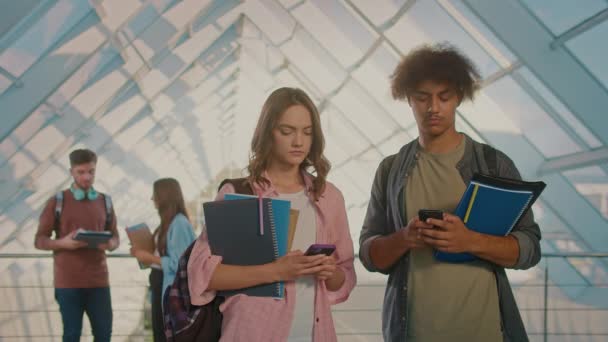 魅力的な2人の学生が大学の廊下で話してスマートフォンを使用しています デジタル教育 将来の技術 チームワーク — ストック動画
