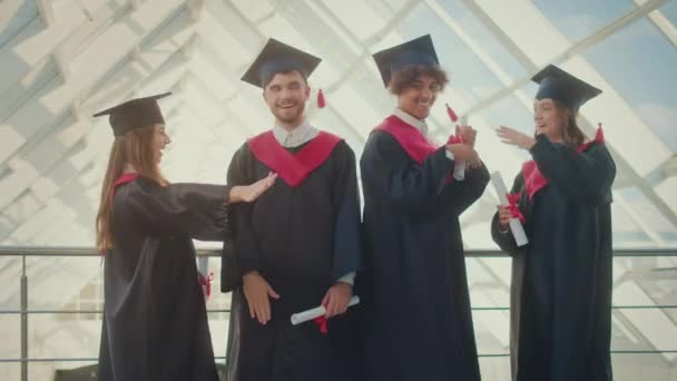 Retrato Grupo Positivo Cuatro Graduados Con Diplomas Abrazándose Juntos Pasillo — Vídeo de stock