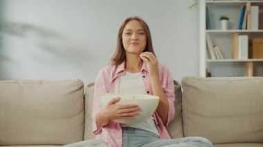 Koltukta oturan, patlamış mısır yiyen ve televizyon izleyen mutlu bir genç kadın. Neşeli Kadın Komik Bir Film İzlerken Güler. Bir Rahatlama ve Psikolojik Rahatlama Biçimi olarak filmler. Çevrimiçi Sinema.