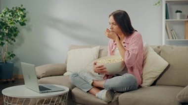 Patlamış mısır yiyen ve dizüstü bilgisayardaki filmi izlemeye odaklanan genç bir kadın. Kanepede oturan ve çok ilginç bir film izleyen ciddi bir kadın. Film Türleri ve Duygusal Tepkiler.
