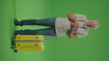 Dikey Görünüm. Yeşil Ekran. Havalimanında elinde sarı bavuluyla bekleyen, Yaşlıları Bekleyen Hayal kırıklığına uğramış yaşlı bir adam..