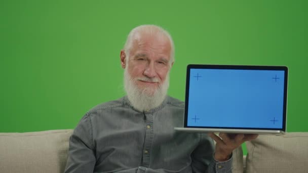 緑の画面 ブルースクリーン付きのラップトップを持つ老人の肖像画は Okサインが表示されます ソファに座って 高齢者のための人工知能と機械学習 — ストック動画