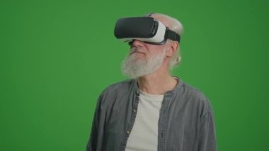 Yeşil Ekran. VR gözlüklü, gri sakallı yaşlı bir adam etraftaki her şeyi inceler. Yaşlılar için Sanal Gerçeklik Eğitimi.