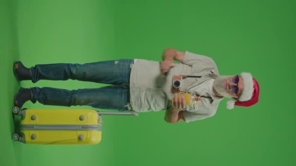 縦表示 緑の画面 スーツケースを着たサンタ ハットの老人 面白いメガネとカクテルの幸せな高齢者は 彼の旅行を楽しみにしています 高齢者の親戚と一緒に旅行する — ストック動画