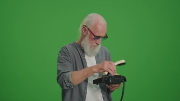 绿色屏风 一个留着灰胡子和滑稽眼镜的老人正在用老式电话交谈 收集及保存旧电话机 — 图库视频影像