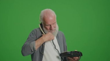 Yeşil Ekran. Gri Sakallı Yaşlı Adam Birisiyle Eski Telefon ve Quarrels Konuşuyor. Eski Telefonları Topluyor ve Koruyor.
