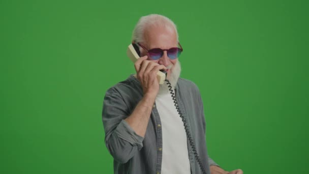 绿色屏风 一个留着灰胡子和滑稽眼镜的老人正在用老式电话交谈 还在和别人争吵 收集和保存老旧的电话 — 图库视频影像