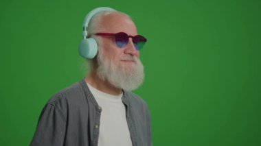 Yeşil Ekran. Komik Gözlüklü Modern Yaşlı Adam Kulaklıkla Müzik Dinliyor ve Dans Ediyor. Yaşlılar için Gelişen Teknolojiler.