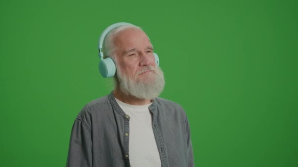 緑の画面 灰色の髭を持つ幸せな老人は ヘッドフォンで音楽を聴く 高齢者向け新技術 — ストック動画