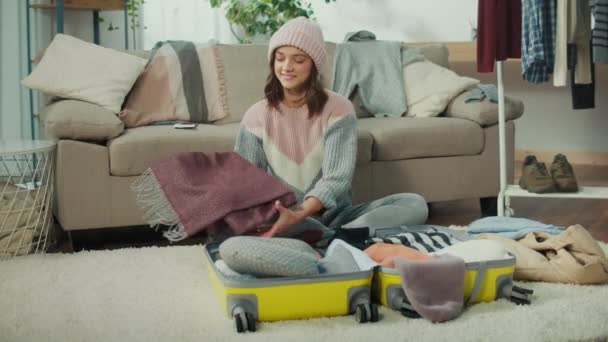 帽子の中の笑顔の若い女性旅行者は旅行のために服を集め 家でスーツケースに物事を詰め込みます 地元の経験 ハイキングとキャンプ — ストック動画