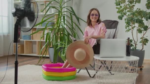 戴着太阳镜和海滩帽的可悲的年轻女性在家庭中在线工作 梦想着度假 在笔记本电脑上工作 坐在扶手椅上 喝苏打水 做度假工作 — 图库视频影像